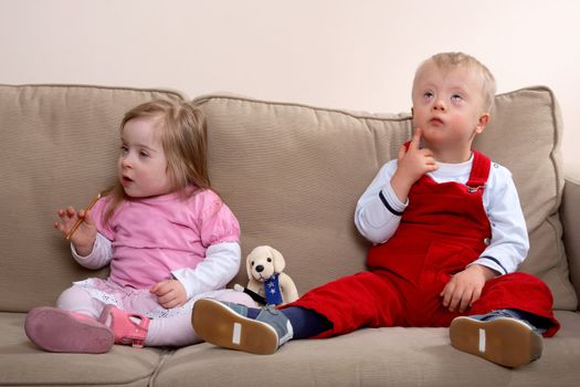 A little boy and girl with Down syndrome sitting on a sofa