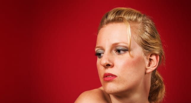 Head portrait of a thoughtful blond girl on red background
