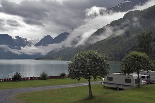 Camping by the mountain lake; mountains and Briksdal glacier at background; cloudy weather, dramatic sky.