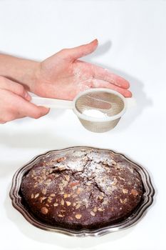 Chocolate cake and sieve with powdered sugar in woman hands
