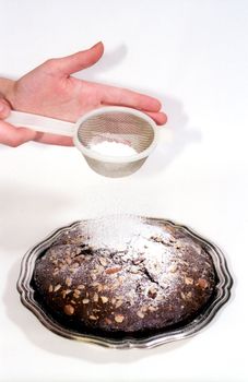 Powdered sugar sprinkling through sieve in woman hands to chocolate cake