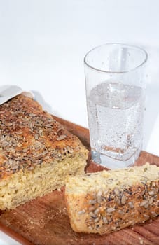 Cutting bread on wooden breadboard and glass of mineral water