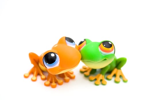 Two plastic frog toys, one orange and one green, isolated on white background.