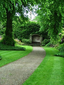 A path through a beautiful garden leading to an ancient garden bench