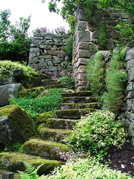 Lichen covered ancient steps lead to a ruined building in a beautiful garden