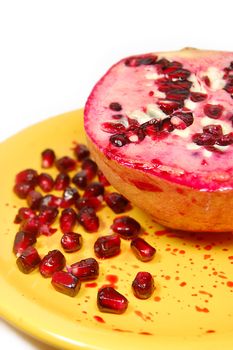 Sliced pomegranate with juice and seeds on yellow plate