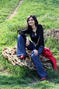 The cheerful girl sits on a stone