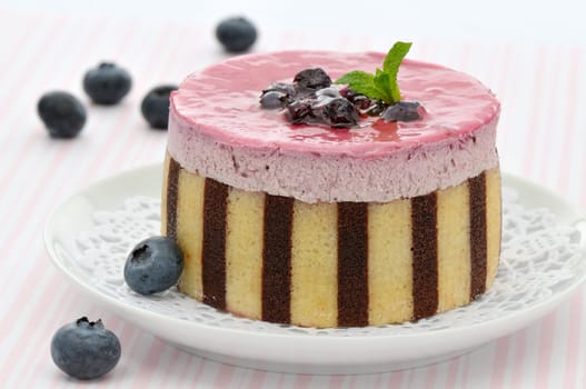 Striped blueberry mousse cake decorated with fruits and mint leaves on a white plate