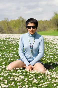 Young sexy lovely woman in sunglasses is posing on the flowering meadow