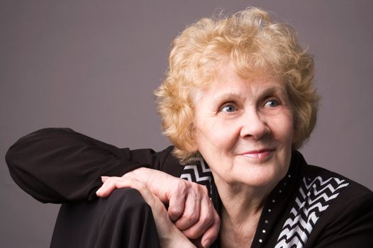 The elderly woman in a black dress on a grey background.