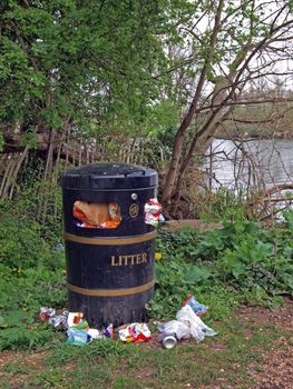 Overfull litter bin, with rubbish on the ground.