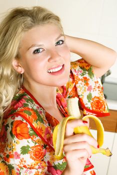 happy beautiful young woman eating a banana at home in the kitchen