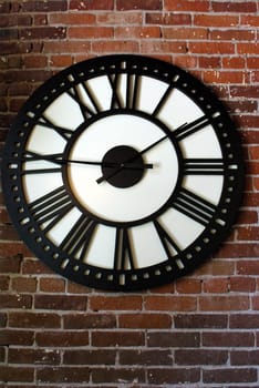 A large outdoor roman numeral clock on a brick wall.