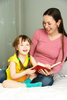 young beautiful mother and her daughter reading a book and laughing