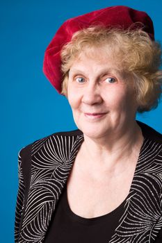 The cheerful elderly woman in red beret on a blue background.