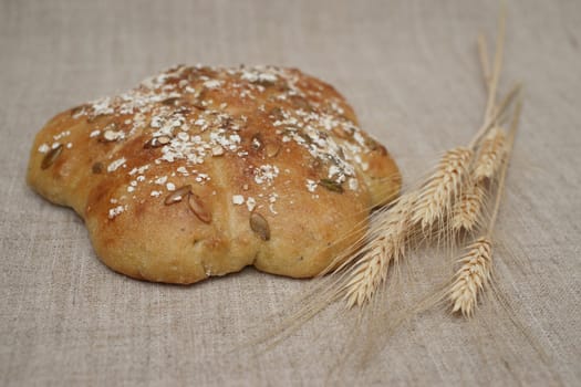 Figured loaf of bread with pepo seeds and wheatears on canvas