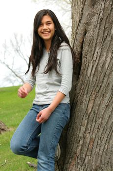 Young teen girl leaning against tree smiling