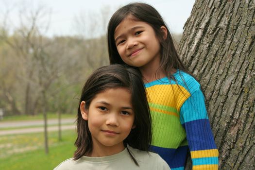 Two little girls standing against tree in spring