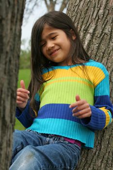 Adorable little girl sitting up against tree
