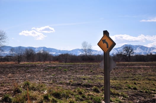 A sign stands in a field with the Rocky Mountains in the distance.