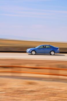 A blue sedan speeds by with the background intentionally blurred due to the movement.