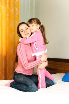 young beautiful mother and her little daughter on the bed at home