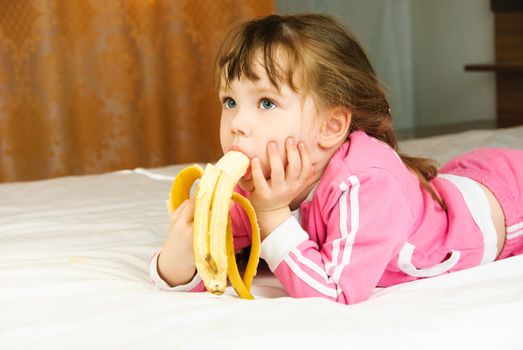 cute little girl eating a banana on the bed at home