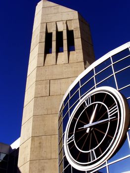 A large modern clock between to towers of contemporary building.