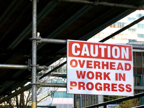 Construction work on scafolding with cation sign.