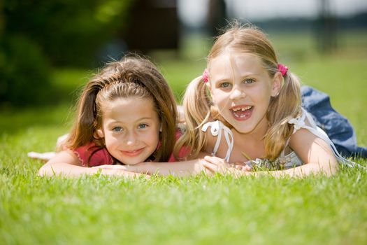 Two young girl lying together in the grass on a summer day