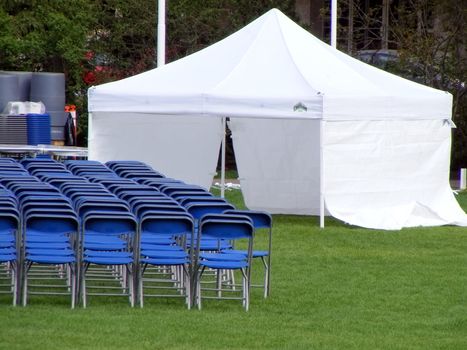 Blue chairs and white tent setup for an outdoor event in the summer time.
