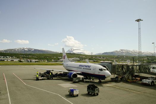 A SAS-Braathens flight getting service before accepting new passengers in Tromsø Airport Langnes. A bright summer day in Tromsø, you can still see snow on the surrounding mountains. 