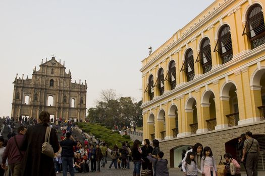 The famous ruins of St. Pauls Cathedral in Macau, a popular tourist attraction and a reminiscence of the old Portugese colonial rule. A lot of tourists are lined up for photos, illustrating the popularity of this landmark.