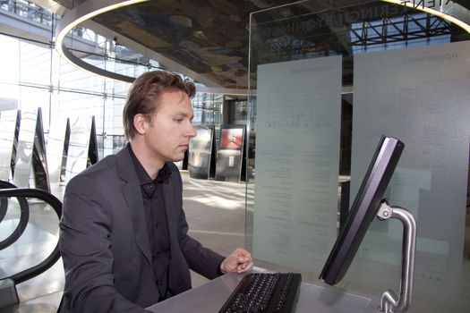 A young executive is standing and using the computer in the in a business lounge