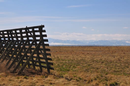 A fence stands in a field with the Rocky Mountains in the distance.