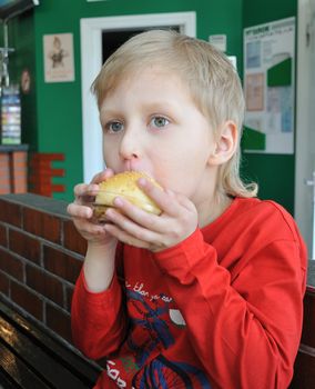 Little boy is eating a baked roll