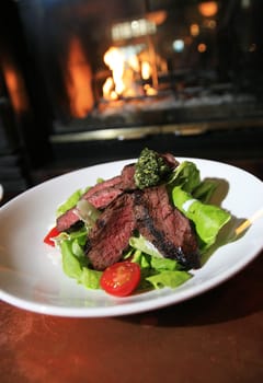 A Bison Steak dish, in front of a fireplace.