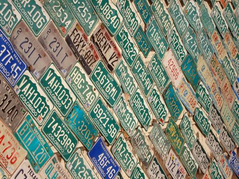 A wall is covered with different color license plates.