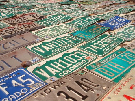 A wall has many different styles of license plates nailed to it.