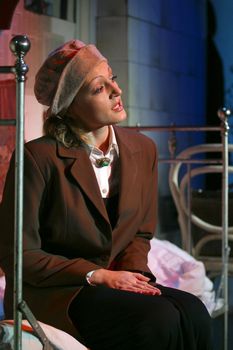 The actress plays a role, sits on old bed on a stage