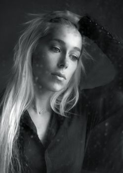 Woman with sad smile behind a wet window. b/w