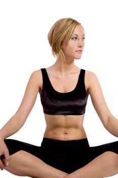 A blond young woman in a fitness outfit is sitting in a lotus position doing yoga