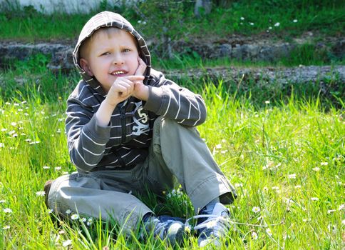 boy sits on the camomile forest meadow and points right