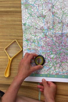 hands of middle aged woman with compass and magnifier glass over map of Greater London, planning next trip