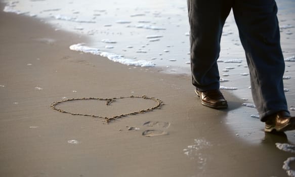 Heart drawn on sand and passing by the man