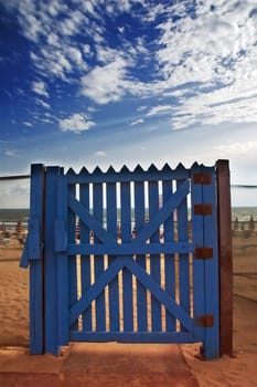 Blue gate on beach with dramatic sky