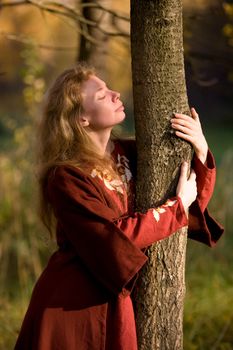 The blonde girl in medieval red dress in the autumn forest
