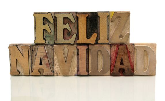 the words 'feliz navidad' in old wood type isolated on white with a reflection