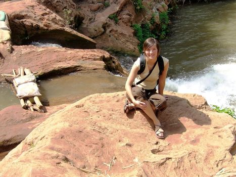 a beautiful woman is sitting on a rock beside a waterfall in Morocco