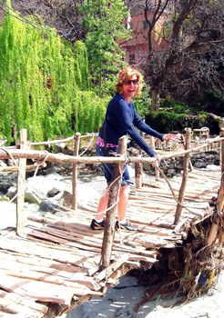 a woman is scared of crossing an unstable bridge over a river.